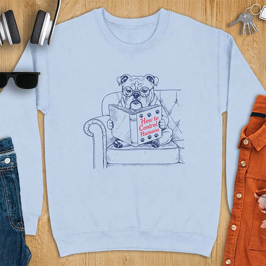 Light Blue sweatshirt with a graphic of a bespectacled English Bulldog sitting in a tufted armchair reading a book titled How to Control Humans, decorated with paw prints