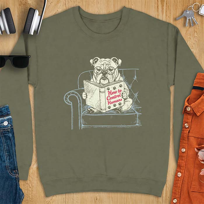 Military Green sweatshirt with a graphic of a bespectacled English Bulldog sitting in a tufted armchair reading a book titled How to Control Humans, decorated with paw prints