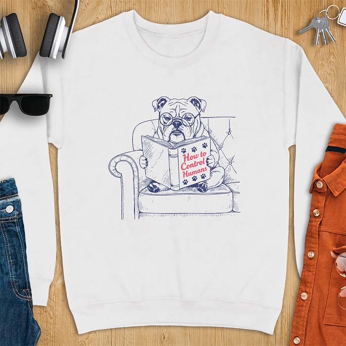 White sweatshirt with a graphic of a bespectacled English Bulldog sitting in a tufted armchair reading a book titled How to Control Humans, decorated with paw prints