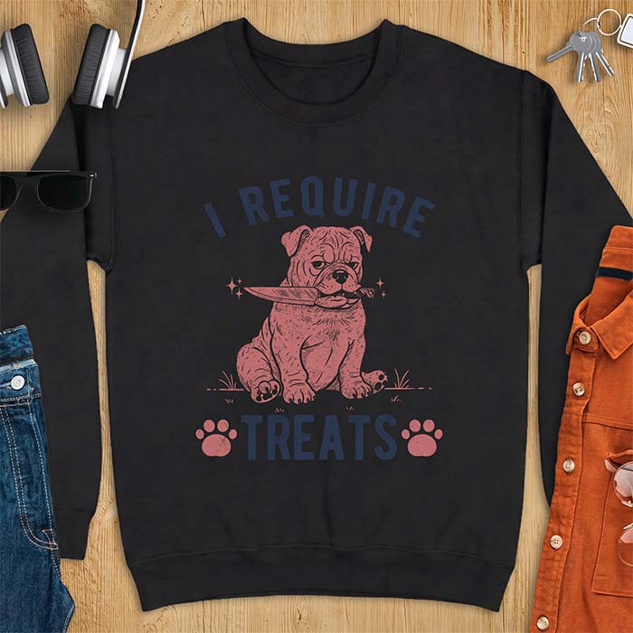 Black sweatshirt with a graphic of a deadpan English Bulldog puppy sitting in grass holding a knife in its mouth, with the text I Require Treats and two paw prints