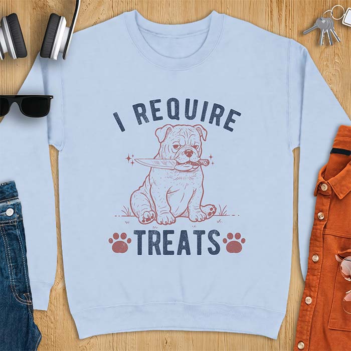 Light Blue sweatshirt with a graphic of a deadpan English Bulldog puppy sitting in grass holding a knife in its mouth, with the text I Require Treats and two paw prints