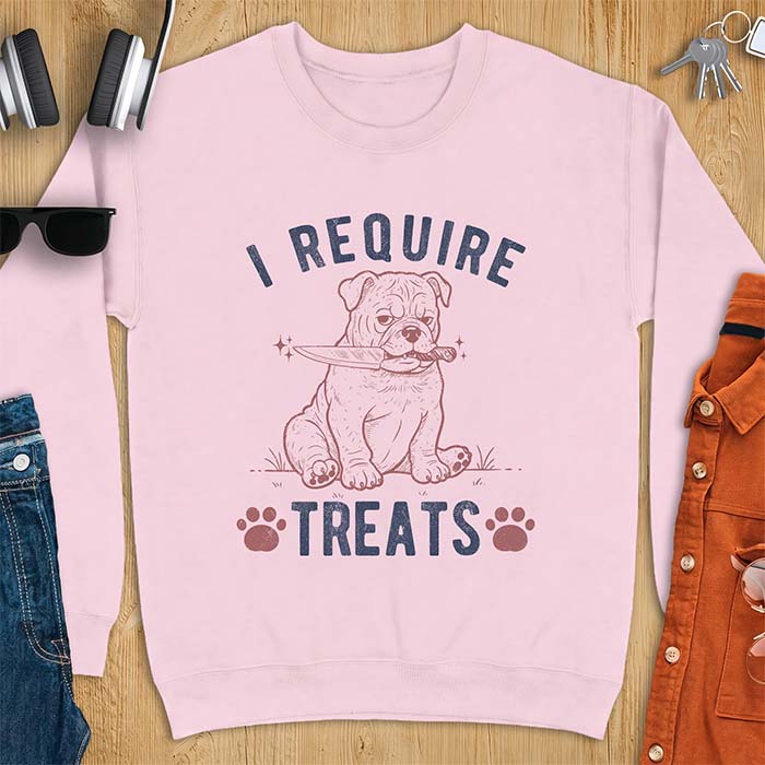 Light Pink sweatshirt with a graphic of a deadpan English Bulldog puppy sitting in grass holding a knife in its mouth, with the text I Require Treats and two paw prints