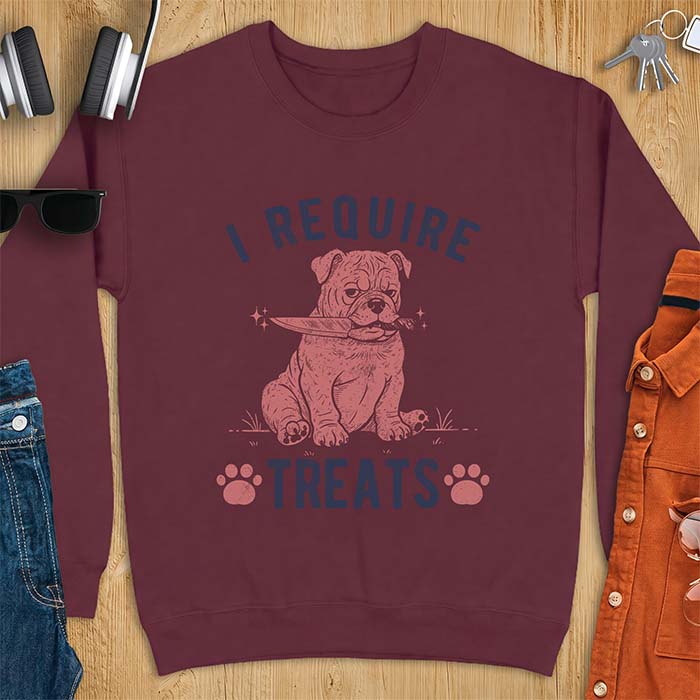 Maroon sweatshirt with a graphic of a deadpan English Bulldog puppy sitting in grass holding a knife in its mouth, with the text I Require Treats and two paw prints
