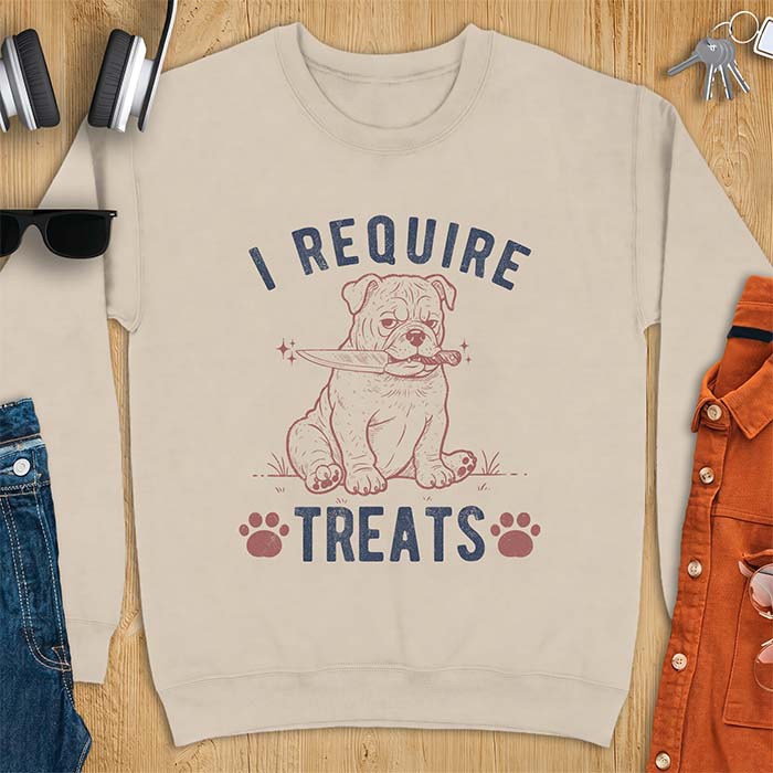 Sand sweatshirt with a graphic of a deadpan English Bulldog puppy sitting in grass holding a knife in its mouth, with the text I Require Treats and two paw prints