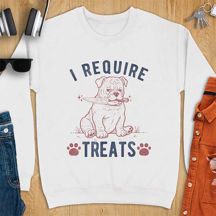 White sweatshirt with a graphic of a deadpan English Bulldog puppy sitting in grass holding a knife in its mouth, with the text I Require Treats and two paw prints