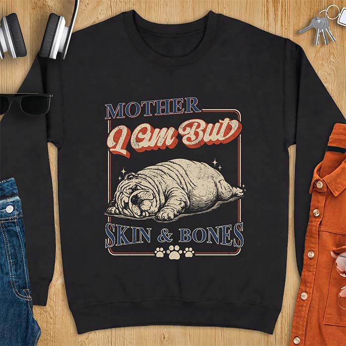 Black sweatshirt with a graphic of an English Bulldog sprawled flat and exhausted, small sparkles floating near its head and the text Mother I Am But Skin & Bones