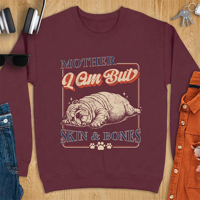 Maroon sweatshirt with a graphic of an English Bulldog sprawled flat and exhausted, small sparkles floating near its head and the text Mother I Am But Skin & Bones