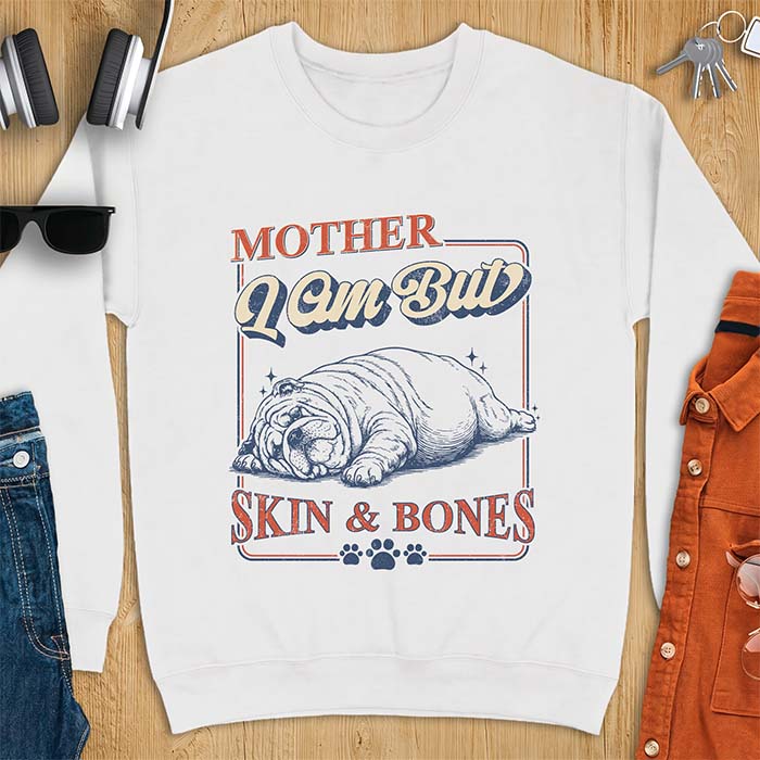 White sweatshirt with a graphic of an English Bulldog sprawled flat and exhausted, small sparkles floating near its head and the text Mother I Am But Skin & Bones