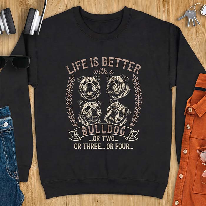 Black sweatshirt with a graphic of four vintage-style bulldog head portraits framed by leafy wreaths and a ribbon banner reading Bulldog, featuring the text Life Is Better With A Bulldog, Or Two, Or Three, Or Four.