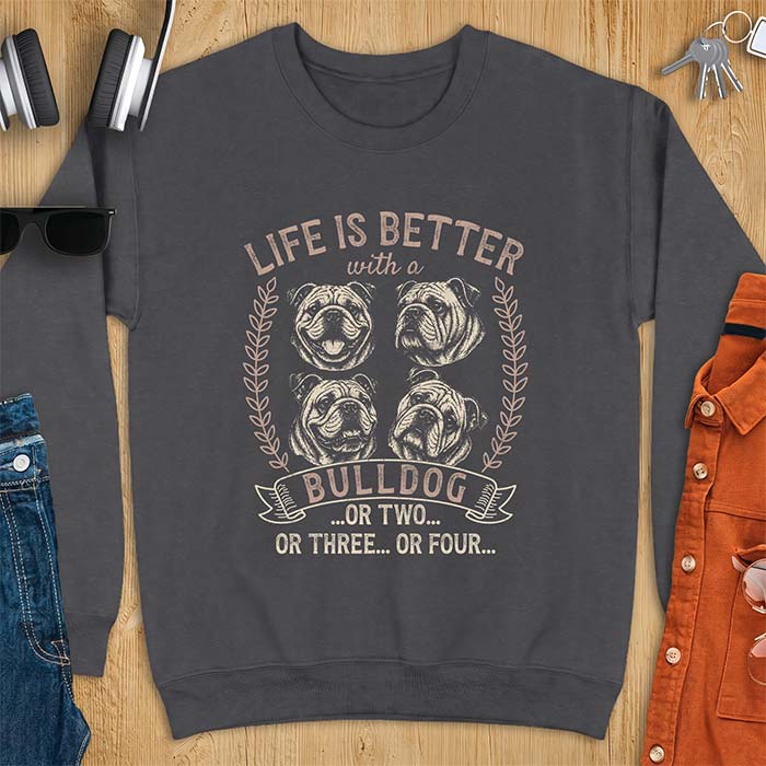 Dark Heather sweatshirt with a graphic of four vintage-style bulldog head portraits framed by leafy wreaths and a ribbon banner reading Bulldog, featuring the text Life Is Better With A Bulldog, Or Two, Or Three, Or Four.