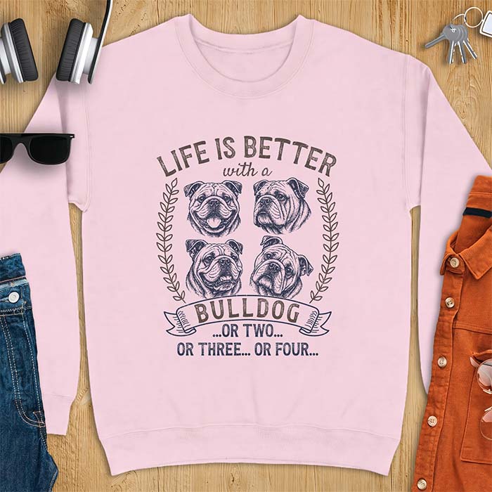 Light Pink sweatshirt with a graphic of four vintage-style bulldog head portraits framed by leafy wreaths and a ribbon banner reading Bulldog, featuring the text Life Is Better With A Bulldog, Or Two, Or Three, Or Four.