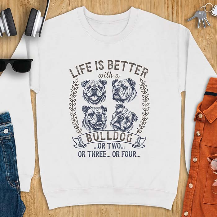 White sweatshirt with a graphic of four vintage-style bulldog head portraits framed by leafy wreaths and a ribbon banner reading Bulldog, featuring the text Life Is Better With A Bulldog, Or Two, Or Three, Or Four.