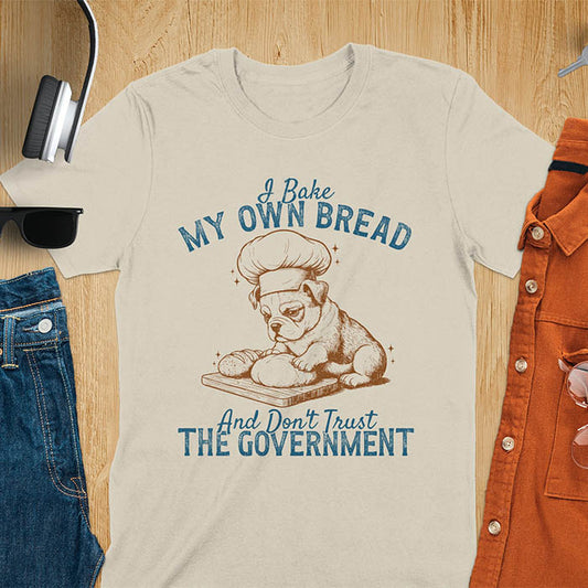 Sand color tee with "I Bake My Own Bread Don't Trust Government" text and vintage bulldog puppy in chef hat kneading bread graphic
