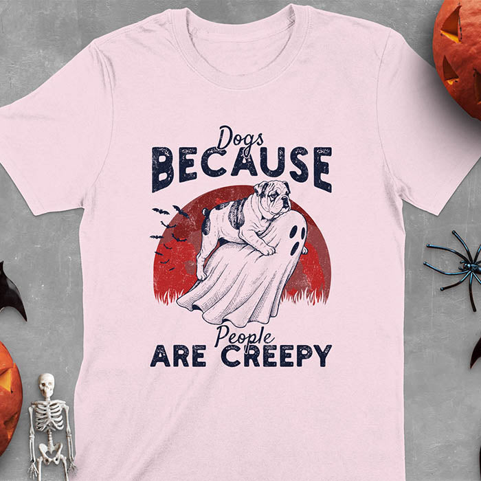 Light pink Halloween t-shirt featuring bulldog riding piggyback on ghost with moon background and bats, text reads 'Dogs Because People Are Creepy'