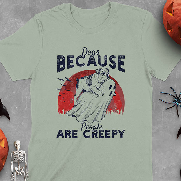 Sage green Halloween t-shirt featuring bulldog riding piggyback on ghost with moon background and bats, text reads 'Dogs Because People Are Creepy'