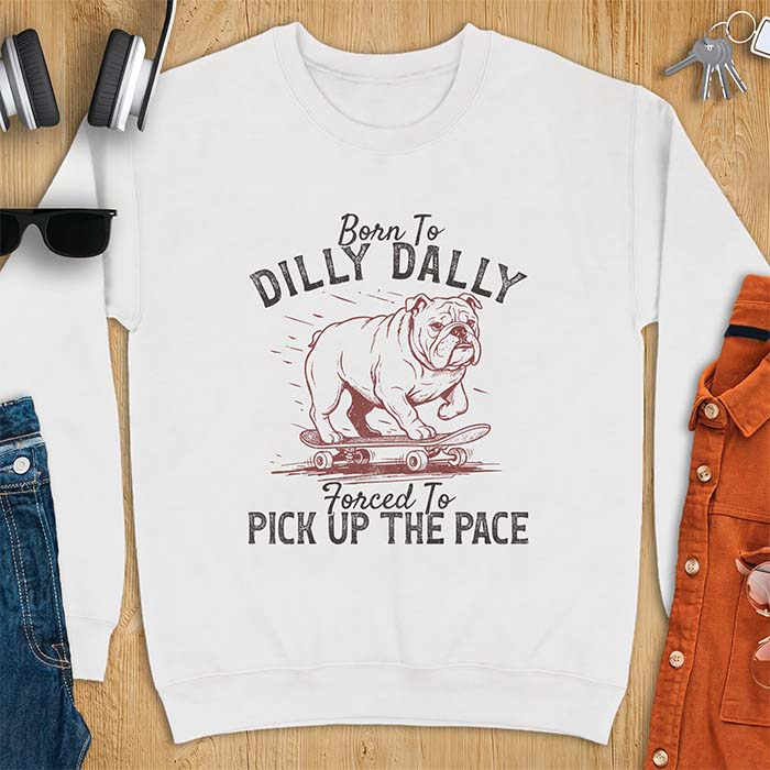 White sweatshirt with a vintage graphic of an English Bulldog riding a skateboard with speed lines behind it and the text Born To Dilly Dally Forced To Pick Up The Pace