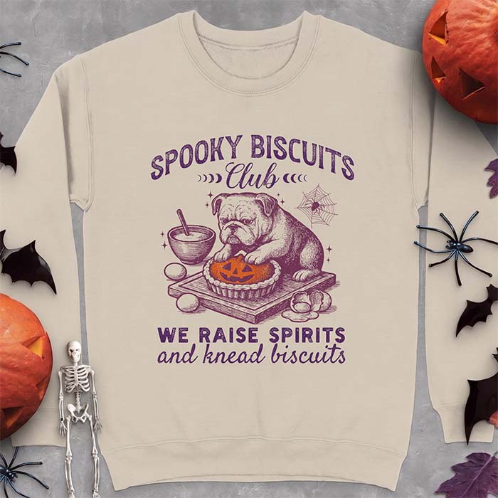 Sand sweatshirt with a Halloween graphic of an English Bulldog puppy making a jack-o-lantern pie with a mixing bowl by the side, the text on the design says Spooky Biscuits Club We Raise Spirits And Knead Biscuits