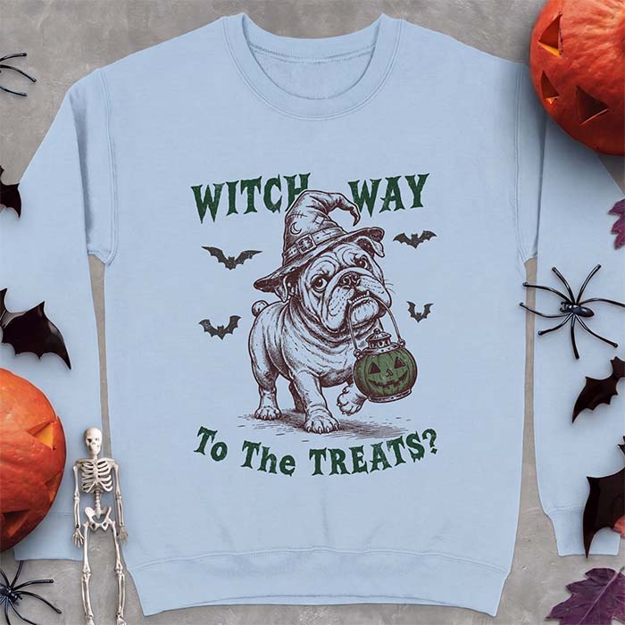 Light Blue sweatshirt with a Halloween graphic of an English Bulldog wearing a patched witch hat carrying a glowing jack-o'-lantern lantern in its mouth with bats flying nearby and the text Witch Way To The Treats?
