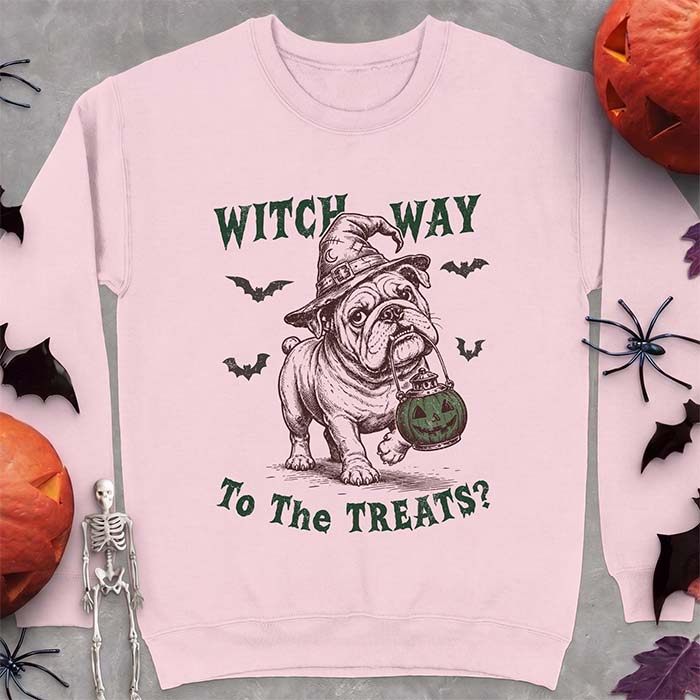 Light Pink sweatshirt with a Halloween graphic of an English Bulldog wearing a patched witch hat carrying a glowing jack-o'-lantern lantern in its mouth with bats flying nearby and the text Witch Way To The Treats?