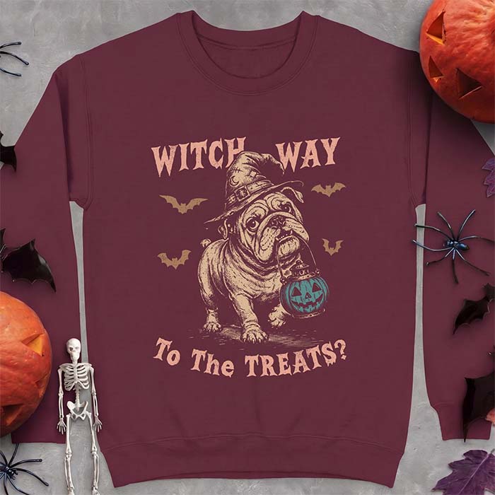 Maroon sweatshirt with a Halloween graphic of an English Bulldog wearing a patched witch hat carrying a glowing jack-o'-lantern lantern in its mouth with bats flying nearby and the text Witch Way To The Treats?