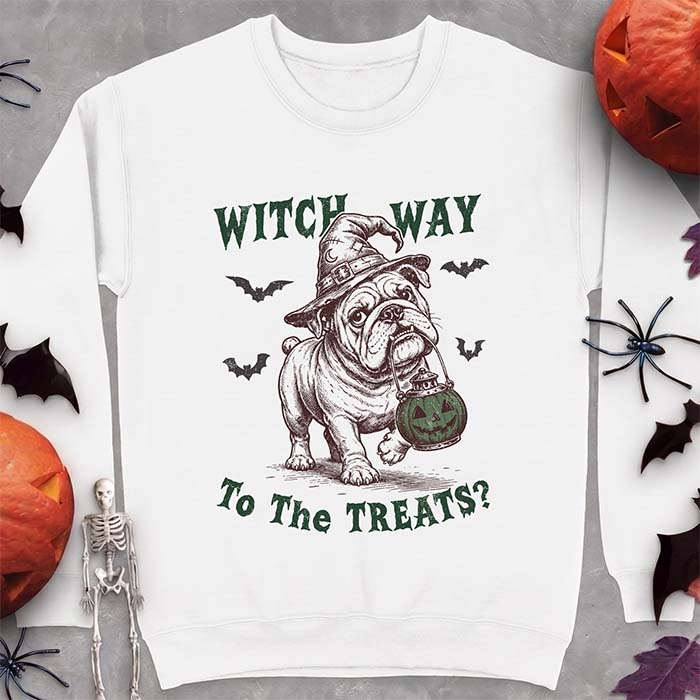 White sweatshirt with a Halloween graphic of an English Bulldog wearing a patched witch hat carrying a glowing jack-o'-lantern lantern in its mouth with bats flying nearby and the text Witch Way To The Treats?