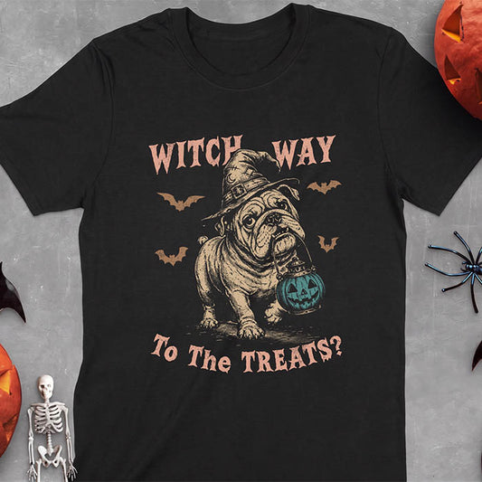 Black t-shirt with a Halloween graphic of an English Bulldog wearing a patched witch hat carrying a glowing jack-o'-lantern lantern in its mouth with bats flying nearby and the text Witch Way To The Treats?