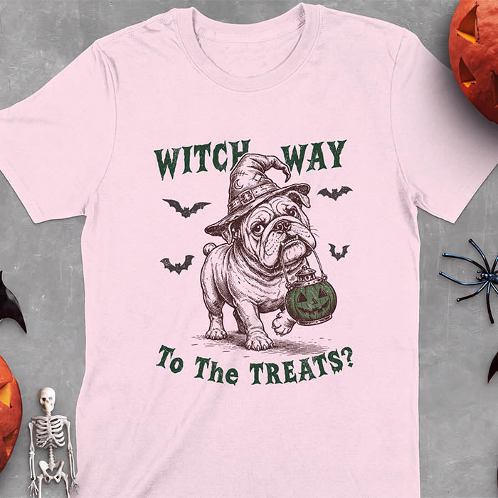 Light Pink t-shirt with a Halloween graphic of an English Bulldog wearing a patched witch hat carrying a glowing jack-o'-lantern lantern in its mouth with bats flying nearby and the text Witch Way To The Treats?