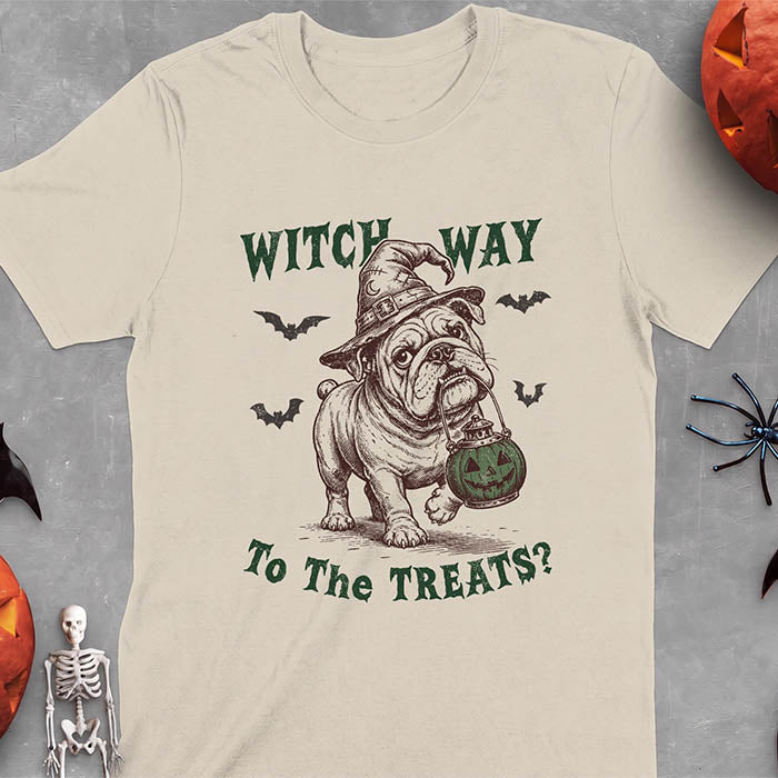 Sand t-shirt with a Halloween graphic of an English Bulldog wearing a patched witch hat carrying a glowing jack-o'-lantern lantern in its mouth with bats flying nearby and the text Witch Way To The Treats?