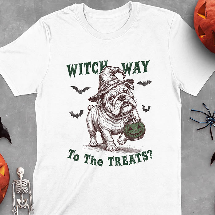 White t-shirt with a Halloween graphic of an English Bulldog wearing a patched witch hat carrying a glowing jack-o'-lantern lantern in its mouth with bats flying nearby and the text Witch Way To The Treats?