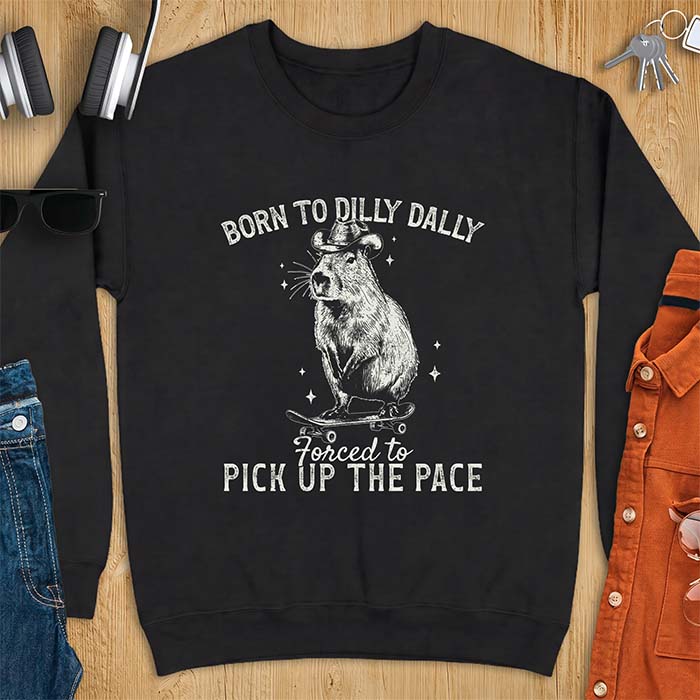 Black sweatshirt with a graphic of a capybara wearing a cowboy hat riding a skateboard surrounded by sparkles, with the text Born To Dilly Dally Forced To Pick Up The Pace