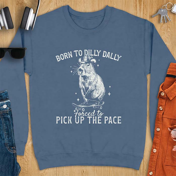 Indigo Blue sweatshirt with a graphic of a capybara wearing a cowboy hat riding a skateboard surrounded by sparkles, with the text Born To Dilly Dally Forced To Pick Up The Pace