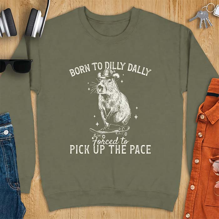 Military Green sweatshirt with a graphic of a capybara wearing a cowboy hat riding a skateboard surrounded by sparkles, with the text Born To Dilly Dally Forced To Pick Up The Pace