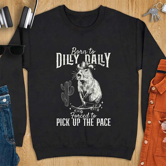 Black sweatshirt with a graphic of a capybara wearing a cowboy hat balanced on a skateboard beside a cactus, plus the text Born to Dilly Dally and Forced to Pick Up The Pace.