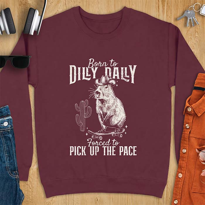 Maroon sweatshirt with a graphic of a capybara wearing a cowboy hat balanced on a skateboard beside a cactus, plus the text Born to Dilly Dally and Forced to Pick Up The Pace.