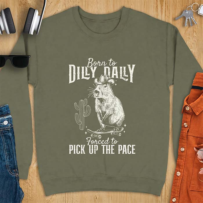 Military Green sweatshirt with a graphic of a capybara wearing a cowboy hat balanced on a skateboard beside a cactus, plus the text Born to Dilly Dally and Forced to Pick Up The Pace.