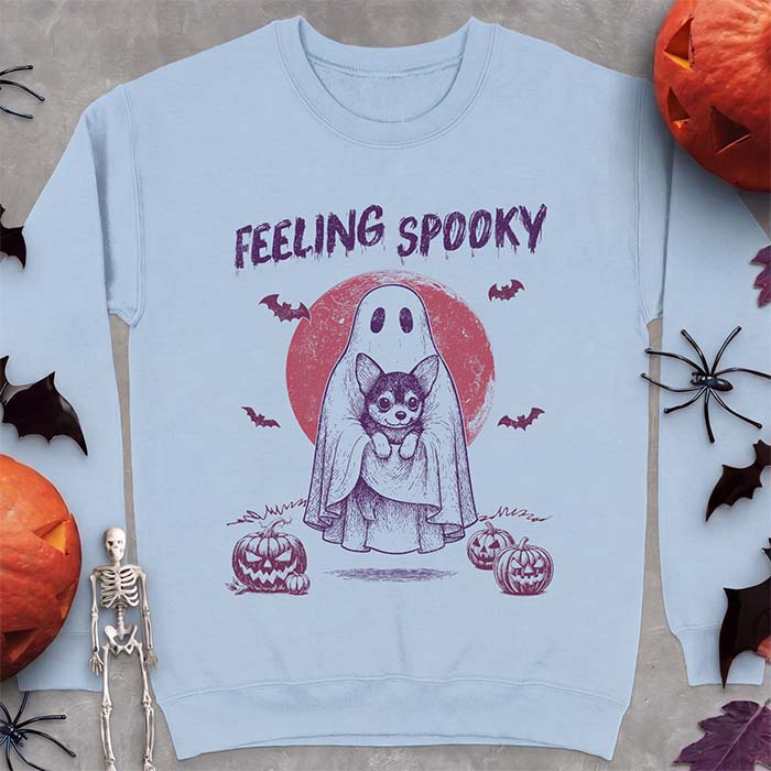 Light Blue sweatshirt with a Halloween graphic of a ghost holding a wide-eyed Corgi puppy in front of a red moon with bats and jack-o-lanterns, with the text Feeling Spooky