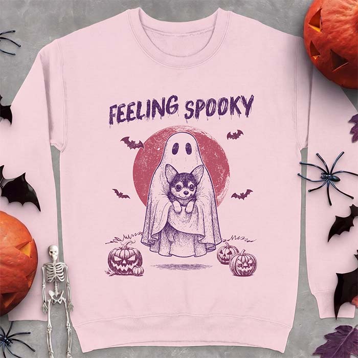 Light Pink sweatshirt with a Halloween graphic of a ghost holding a wide-eyed Corgi puppy in front of a red moon with bats and jack-o-lanterns, with the text Feeling Spooky