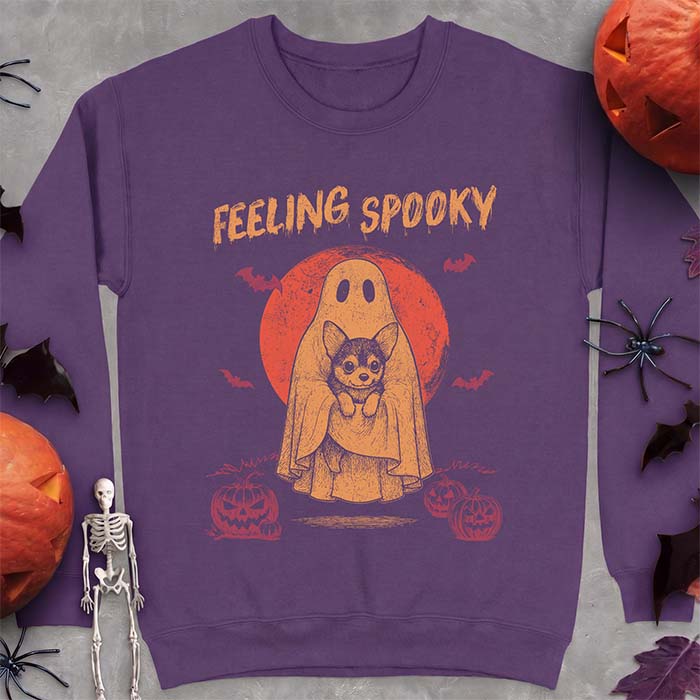 Purple sweatshirt with a Halloween graphic of a ghost holding a wide-eyed Corgi puppy in front of a red moon with bats and jack-o-lanterns, with the text Feeling Spooky