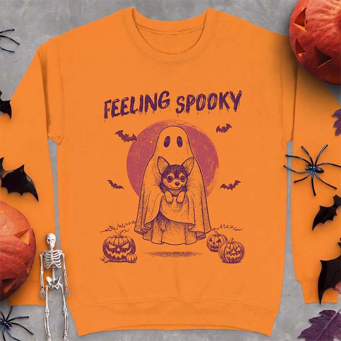 Safety Orange sweatshirt with a Halloween graphic of a ghost holding a wide-eyed Corgi puppy in front of a red moon with bats and jack-o-lanterns, with the text Feeling Spooky