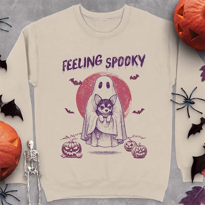 Sand sweatshirt with a Halloween graphic of a ghost holding a wide-eyed Corgi puppy in front of a red moon with bats and jack-o-lanterns, with the text Feeling Spooky