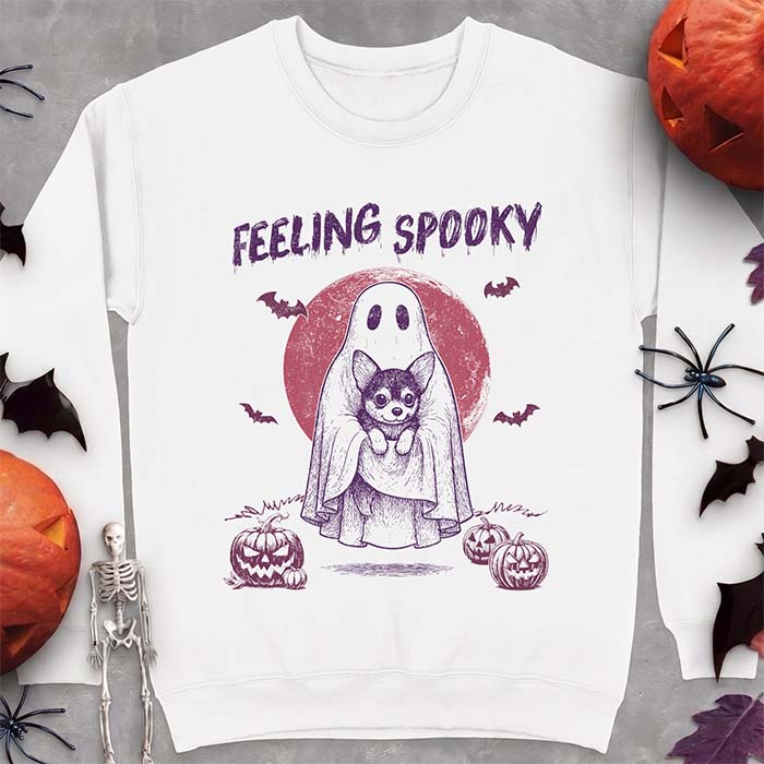 White sweatshirt with a Halloween graphic of a ghost holding a wide-eyed Corgi puppy in front of a red moon with bats and jack-o-lanterns, with the text Feeling Spooky