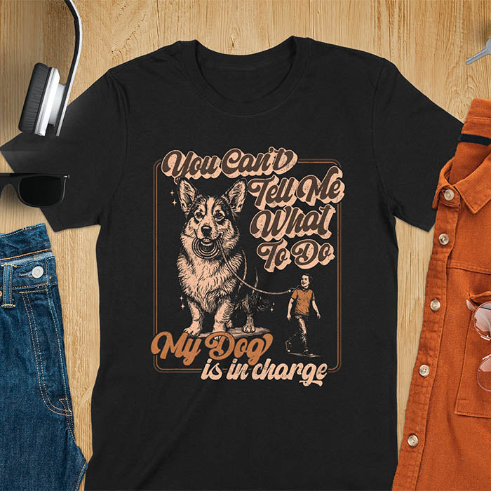You Can't Tell Me What To Do My Dog Is In Charge text with man being walked on leash by corgi in vintage retro frame graphic on black t-shirt