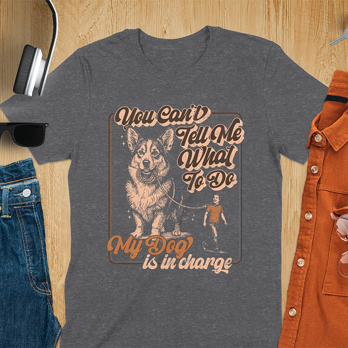 You Can't Tell Me What To Do My Dog Is In Charge text with man being walked on leash by corgi in vintage retro frame graphic on dark heather t-shirt