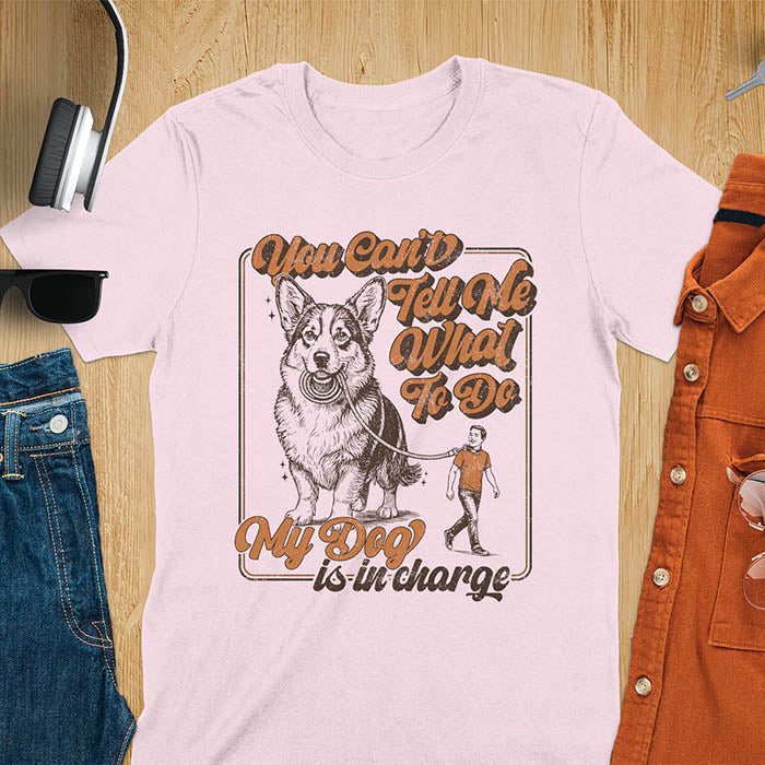 You Can't Tell Me What To Do My Dog Is In Charge text with man being walked on leash by corgi in vintage retro frame graphic on light pink t-shirt