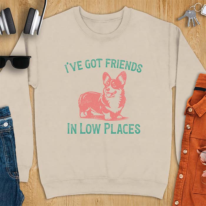 Sand color sweatshirt with a vintage Corgi illustration standing and facing forward, with distressed teal text arched above reading "I'VE GOT FRIENDS" and below reading "IN LOW PLACES.