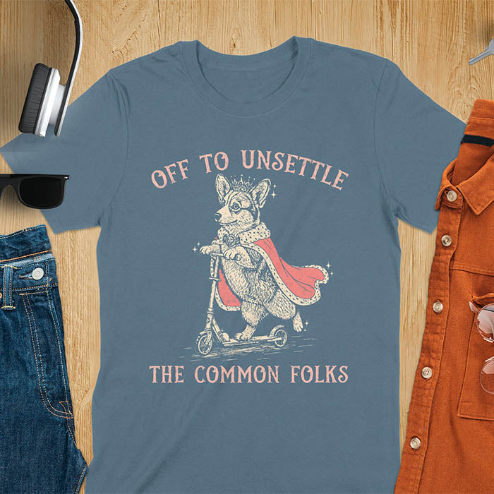 Off To Unsettle The Common Folks text with king corgi wearing crown and red cape on skateboard scooter vintage meme graphic on indigo blue t-shirt