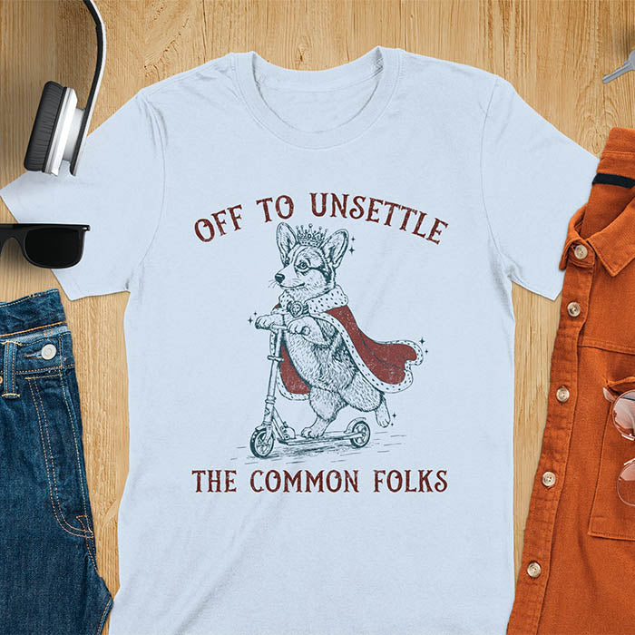 Off To Unsettle The Common Folks text with king corgi wearing crown and red cape on skateboard scooter vintage meme graphic on light blue t-shirt