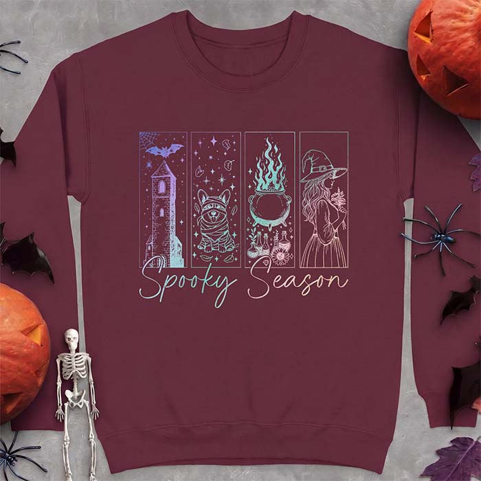 Maroon sweatshirt with a four-panel Halloween graphic of a haunted tower, a bandage-wrapped Corgi mummy, a bubbling cauldron with potion bottles and a witch holding flowers, with the text Spooky Season