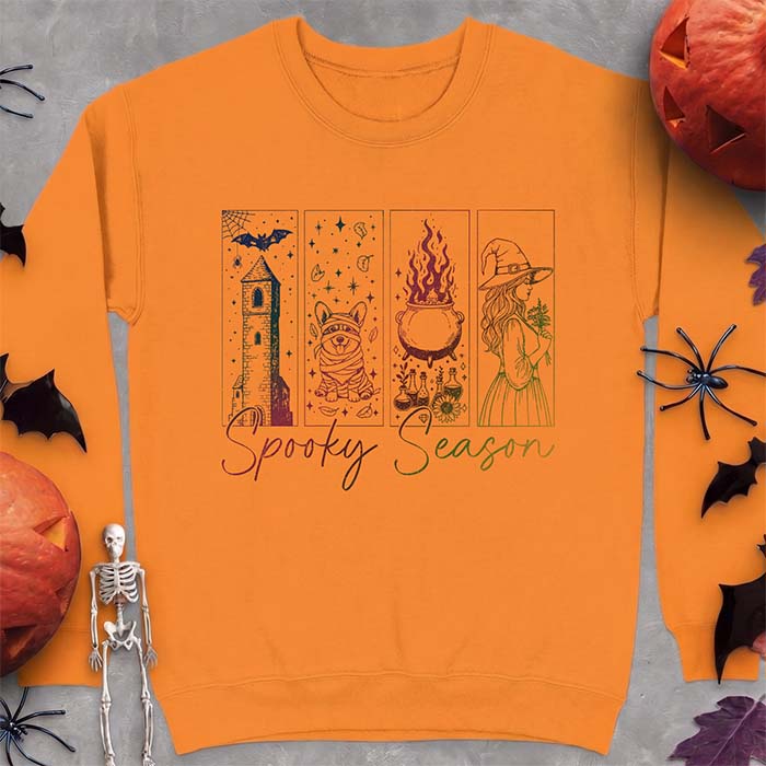 Safety orange sweatshirt with a four-panel Halloween graphic of a haunted tower, a bandage-wrapped Corgi mummy, a bubbling cauldron with potion bottles and a witch holding flowers, with the text Spooky Season