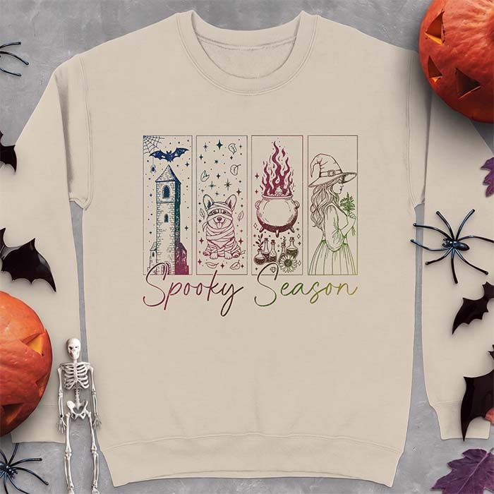 Sand sweatshirt with a four-panel Halloween graphic of a haunted tower, a bandage-wrapped Corgi mummy, a bubbling cauldron with potion bottles and a witch holding flowers, with the text Spooky Season